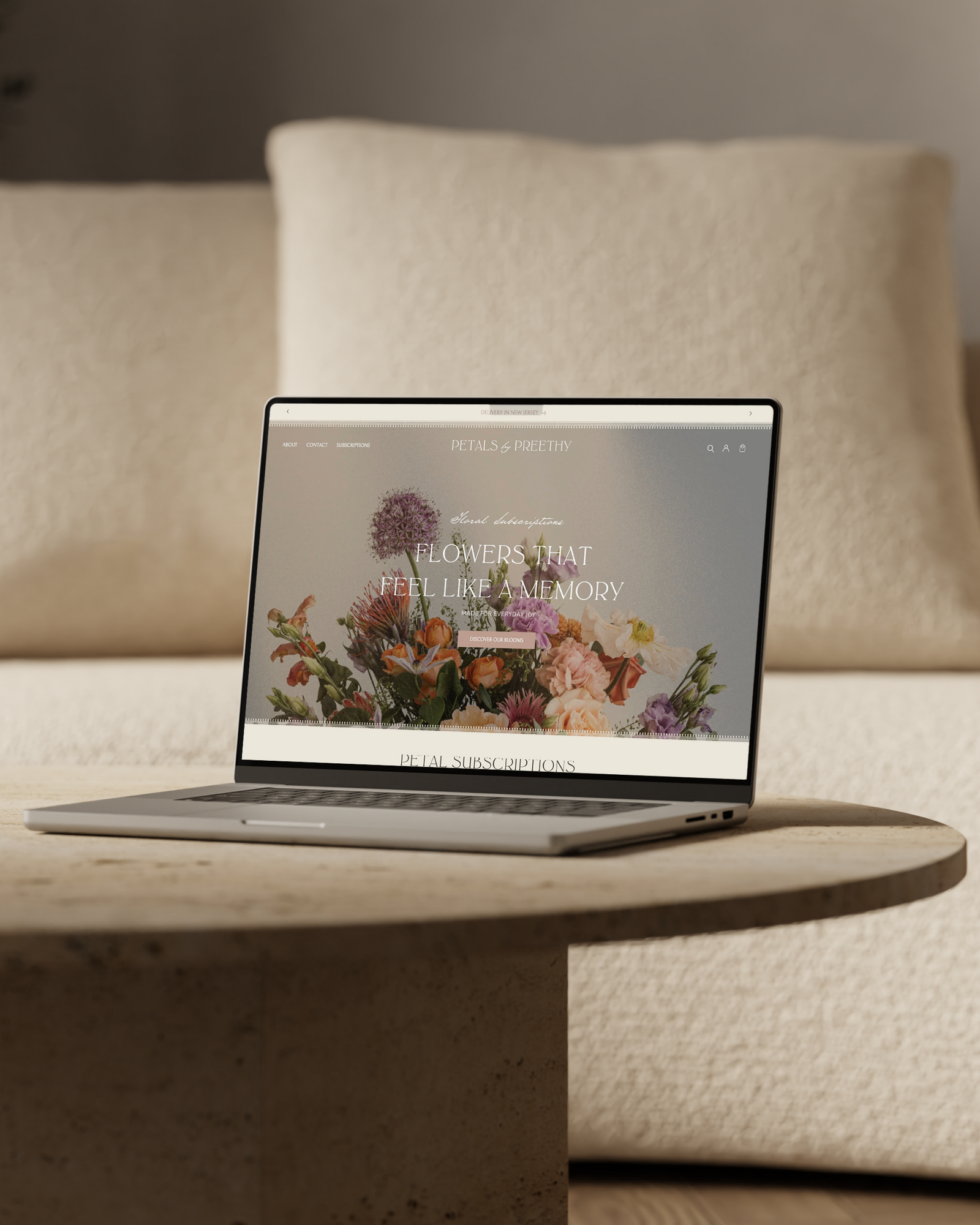 Petals by Preethy Flower Website by Jill and Co shown on a laptop on a coffee table with a floral design on the screen, placed against a beige sofa.